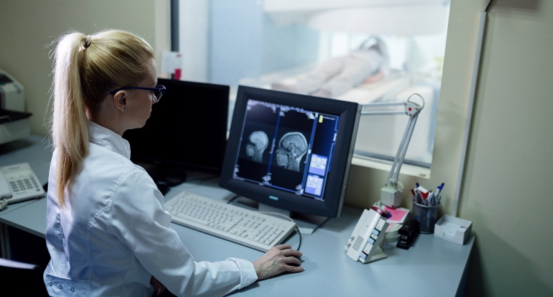 Radiologist analyzing brain MRI scan results of a patient on computer monitor in control room.